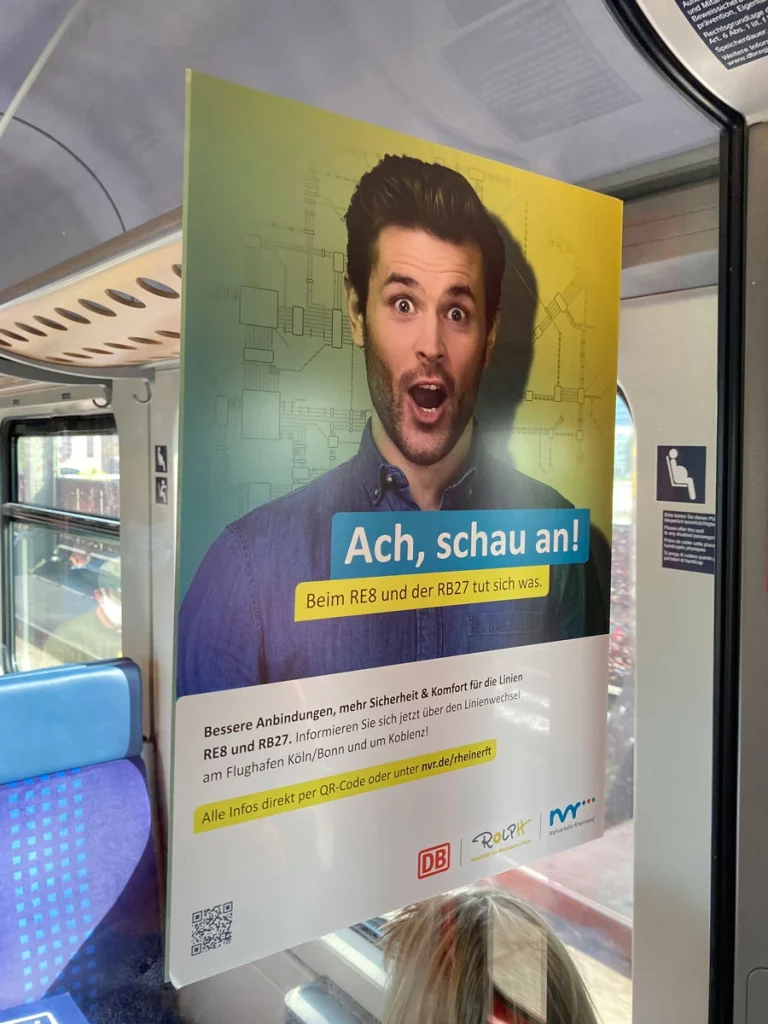 Werbeposter mit überraschter Männermimik im Zug – Kampagnenmotiv für den Nahverkehr Rheinland, fotografiert von nonverbal | businessfotografie.