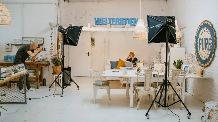 Making-of-Szene aus dem Fotostudio von nonverbal | businessfotografie in Köln: Fotograf bei der Arbeit mit Studioequipment, Kundin am Laptop im Gespräch.