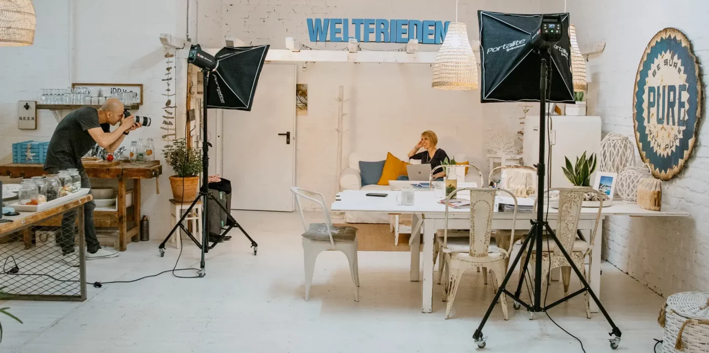 Making-of-Szene aus dem Fotostudio von nonverbal | businessfotografie in Köln: Fotograf bei der Arbeit mit Studioequipment, Kundin am Laptop im Gespräch.